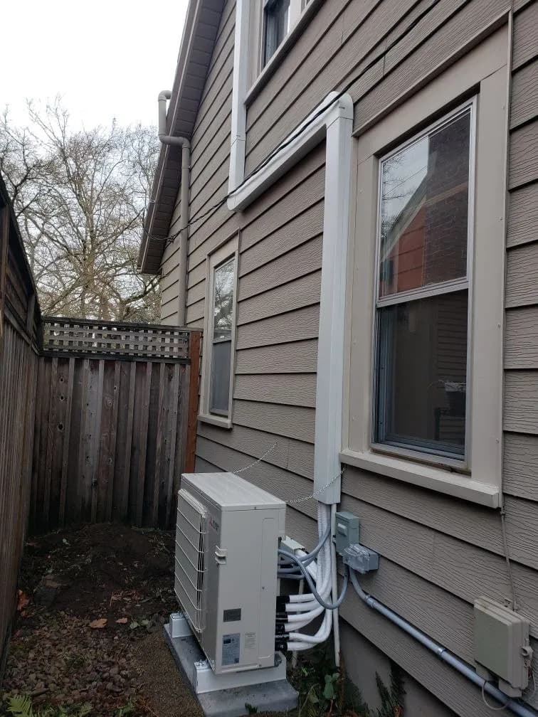 Ductless heat pump outdoor unit with its line-set cover installed beside a home