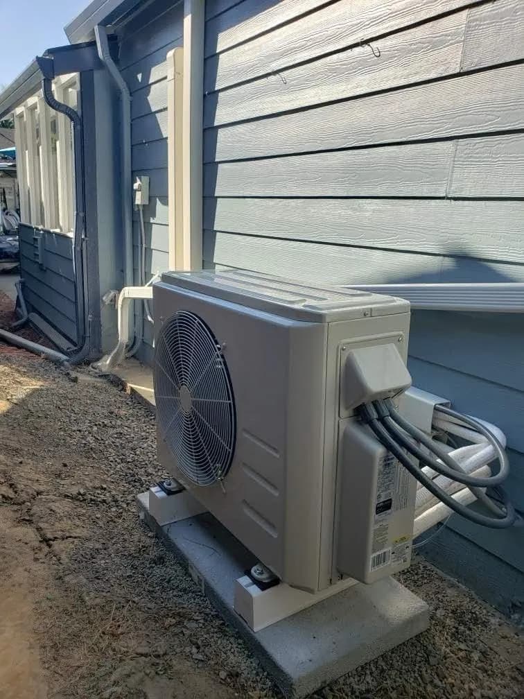 Outdoor heat pump installed on a concrete pad beside a blue home
